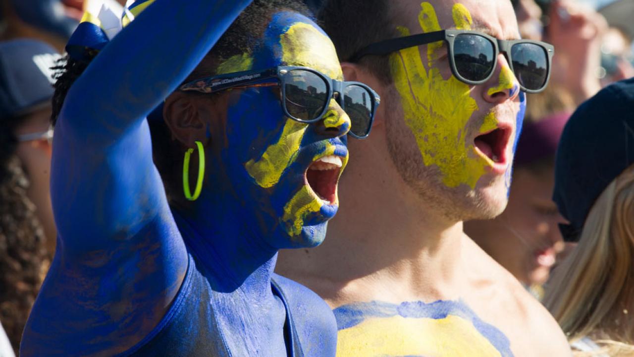a male and female student painted in 鶹Ů blue and gold cheer on the Aggies at the annual homecoming football game